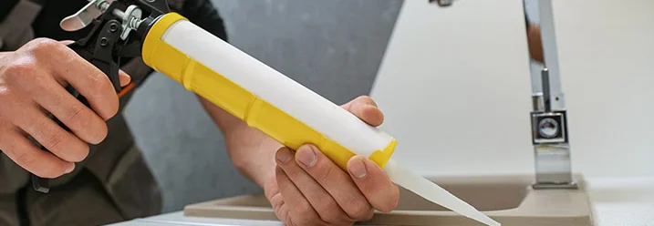 Person versiegelt Spüle mit Silikonpistole